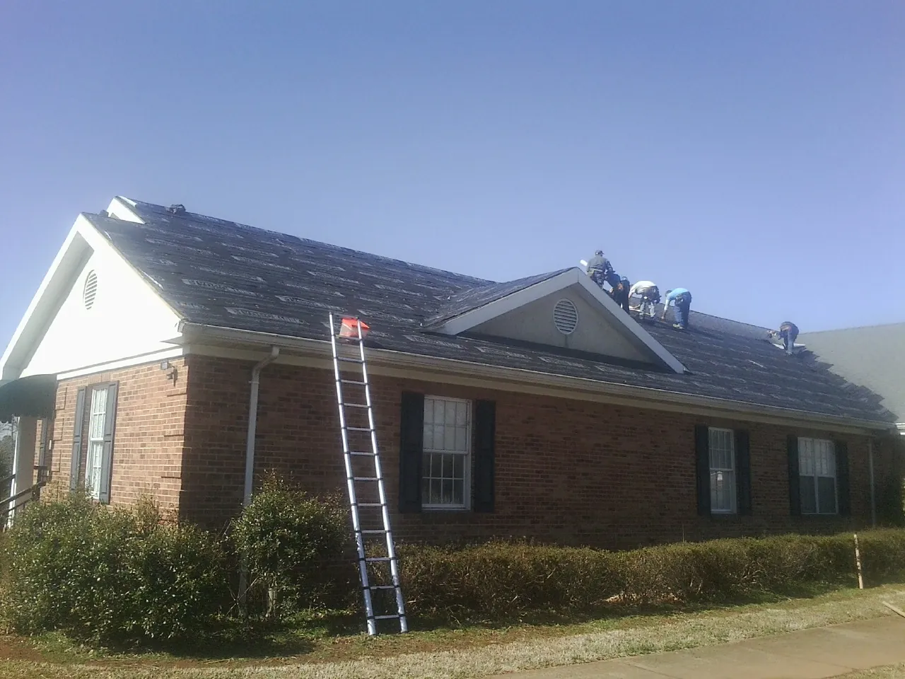 Crew tearing shingles off a brick ranch roof with a ladder set — Emergency Roof Repair work by our crew in Nanjemoy