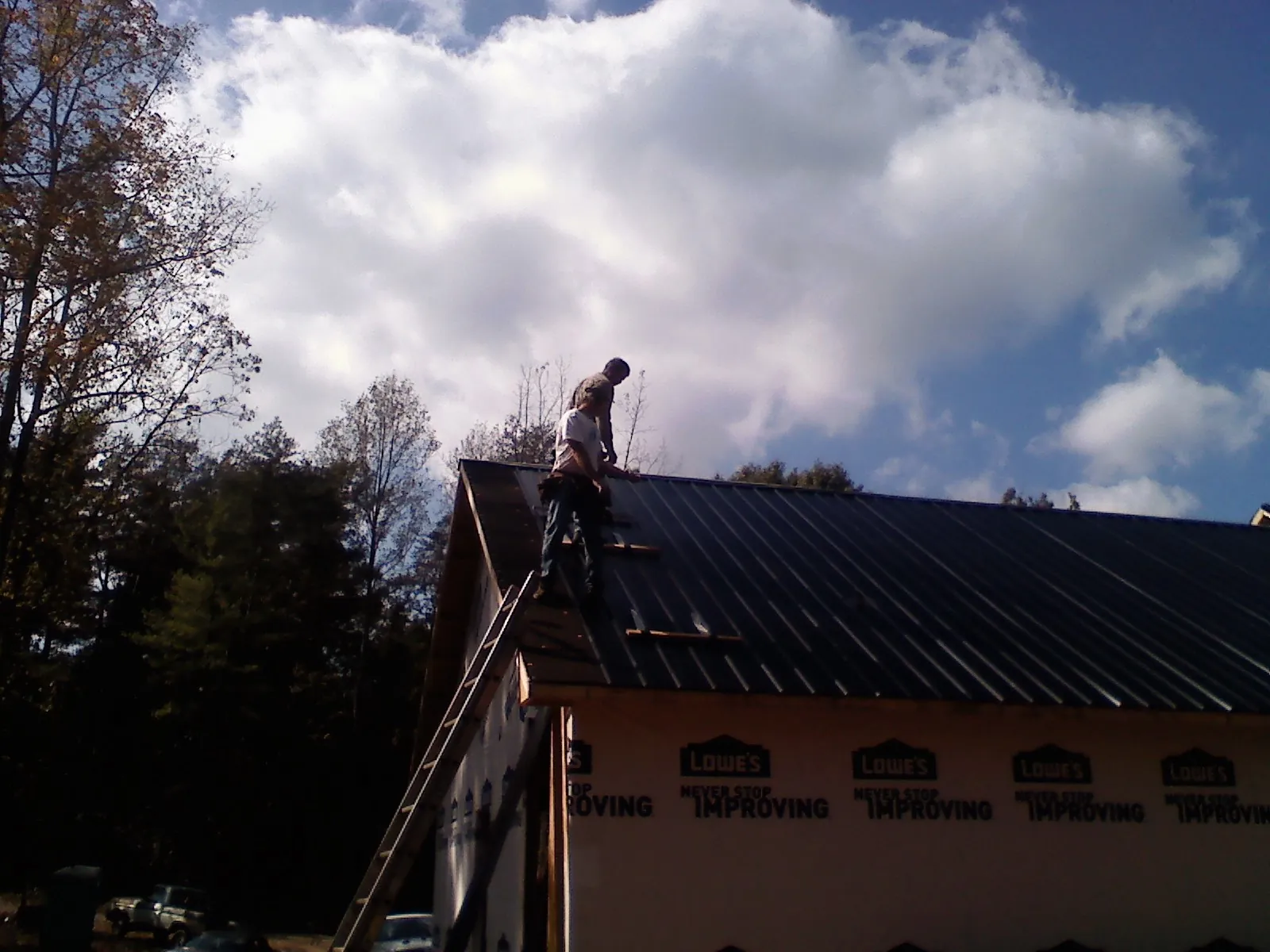 Roofer fastening dark metal panels high against a cloudy sky, from a Roof Inspection job in Nanjemoy
