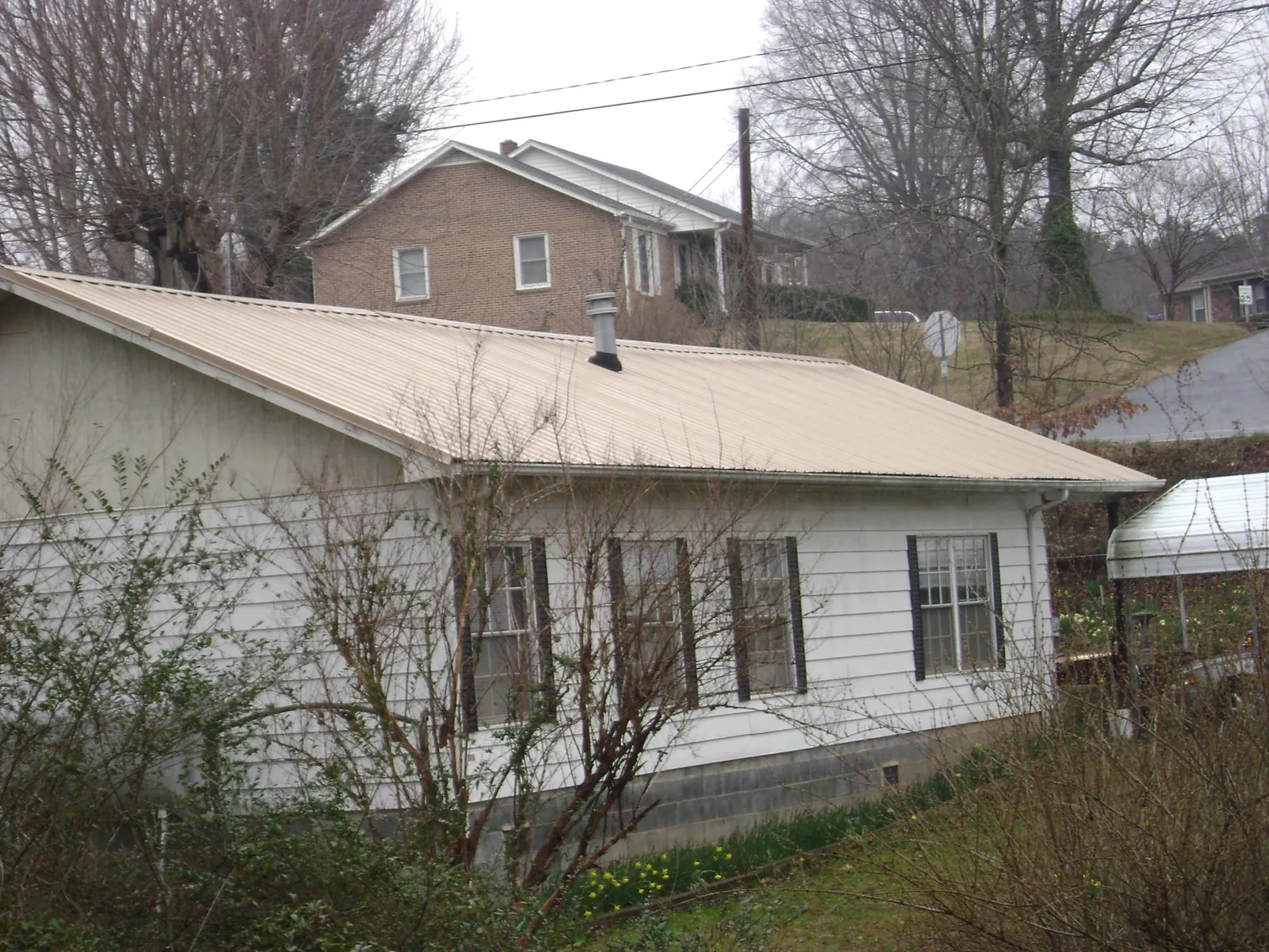 Tan metal roof on a white sided house set into a hillside — Commercial Roofing by Roofing Brothers in Nanjemoy